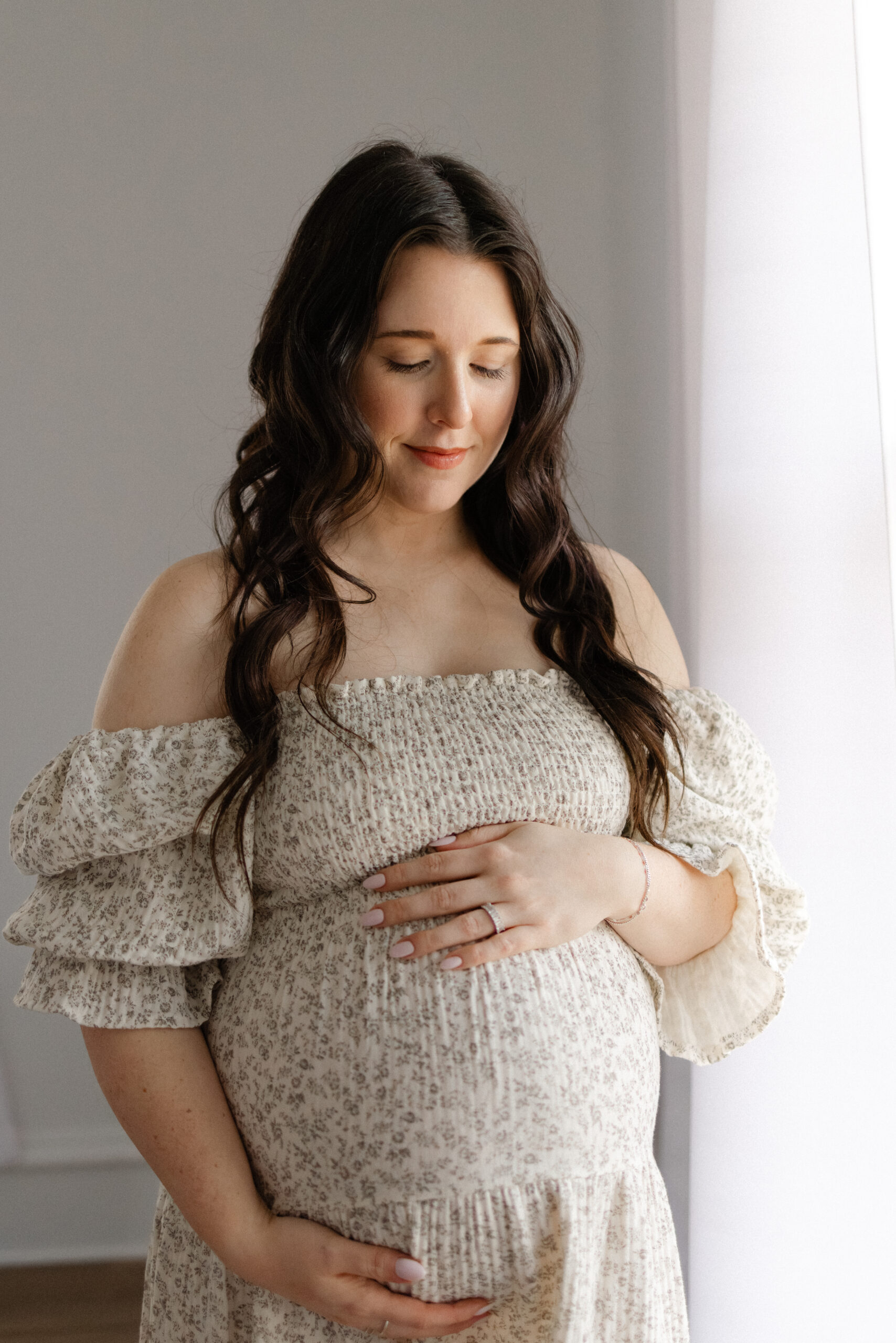 A pregnant woman in soft indoor light gently cradling her baby bump during a maternity photo session